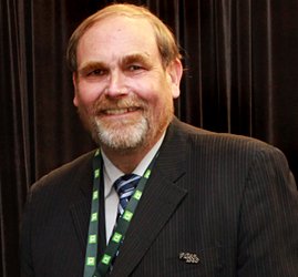 Headshot of a man with a beard wearing a green lanyard and black jacket.