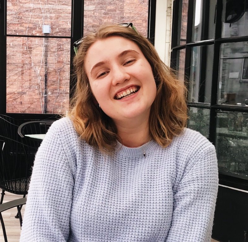 Woman smiling at the camera wearing a light blue sweater and short blonde hair