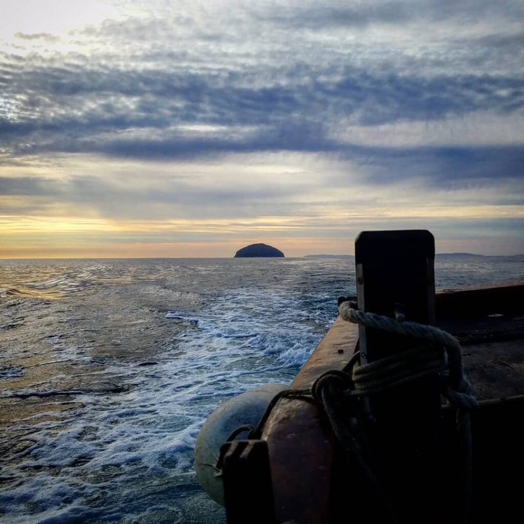 Departing by boat from Ailsa Craig. Ocean stretches into the sunset with a small island in the distance.