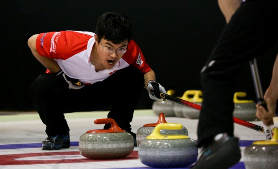 Derek curling. He crouches over the curling stones with his mouth open, as if yelling.