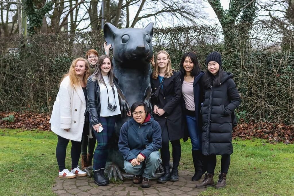 Group of 7 young adults gathered around a statue of a mouse. 