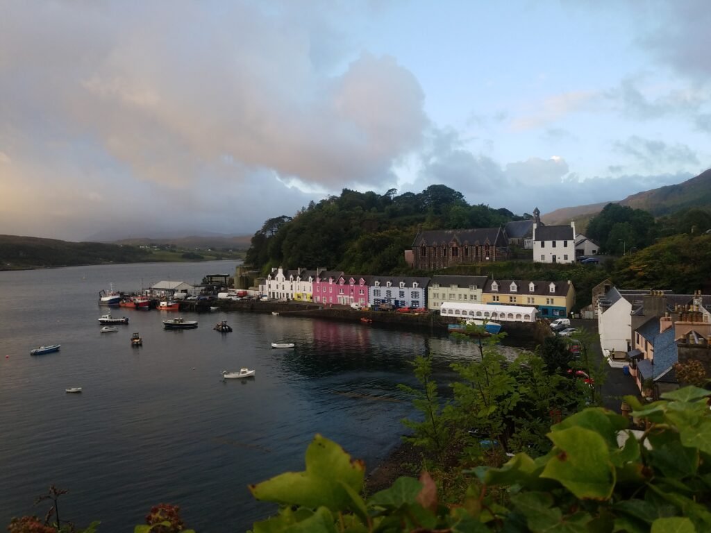 Overlooking Portree harbourfront with dark water, boats, and colourful buildings along the shore.