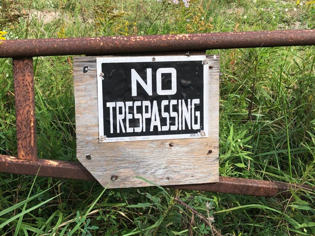 No Trespassing sign posted on a fence in front of long grass