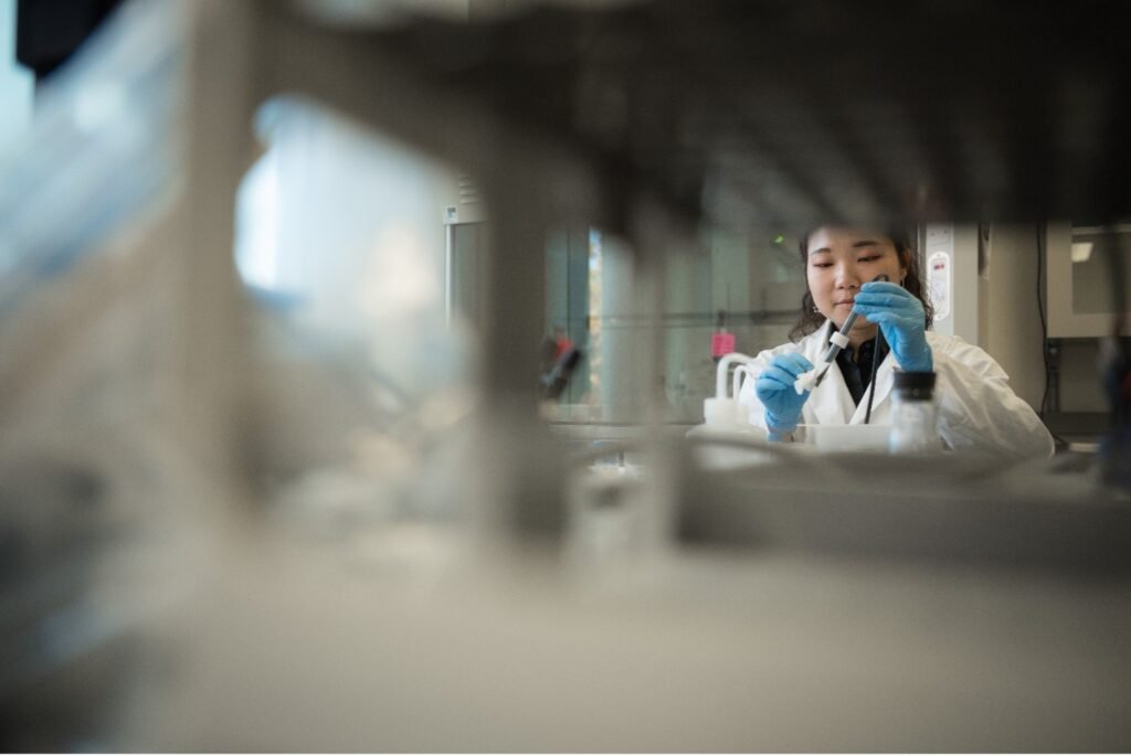 Woman in a lab using glass instruments. Blurred vials are in the foreground and woman is in focus in the background.