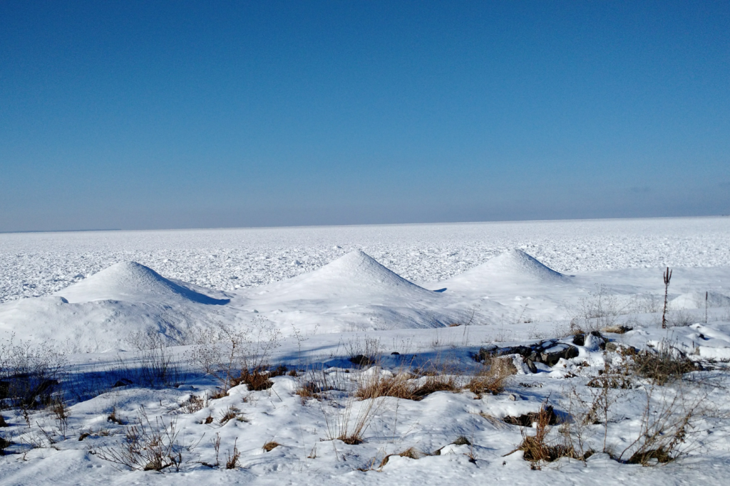 Row of three ice volcanoes along the shore of a frozen lake.
