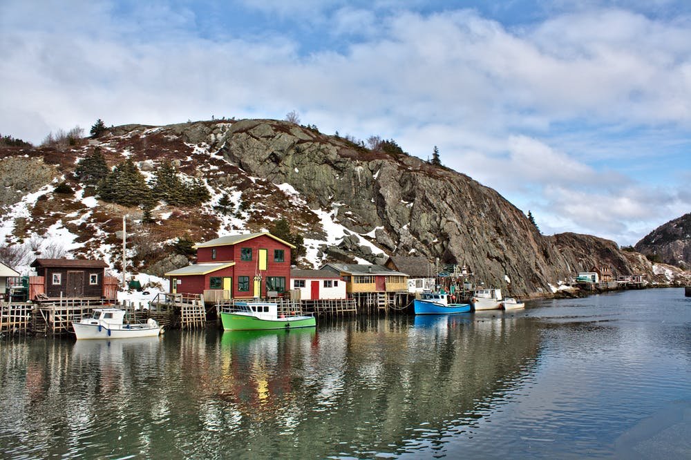 Shoreline in Newfoundland and Labrador showing colourful houses and boats with a rocky hill in the background