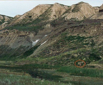 Mountains in the distance with brown peaks and grassy valleys. A red circle has been drawn on the photo encircling Cam in the far distance.