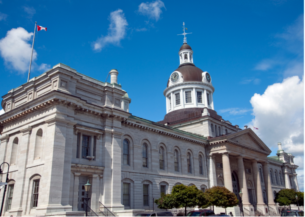 Looking up at city hall, a large building made from white limestone with a central clock tower.