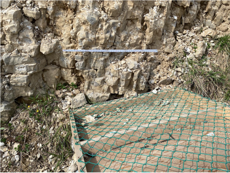 A large tray covered with wire underneath a cliff.