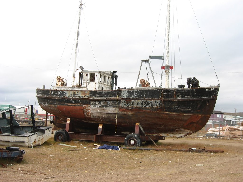 An old boat sitting on a beach. The red and black paint is faded and there is a small white cabin on the deck.