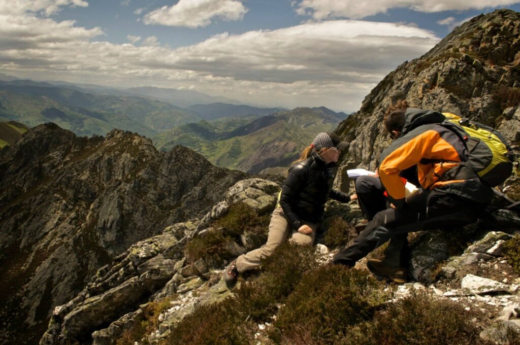 Two people climbing the side of a mountain. In the background more mountains can be seen.