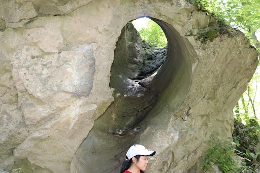 Person standing in front of a tunnel-like feature in a rock outcrop.