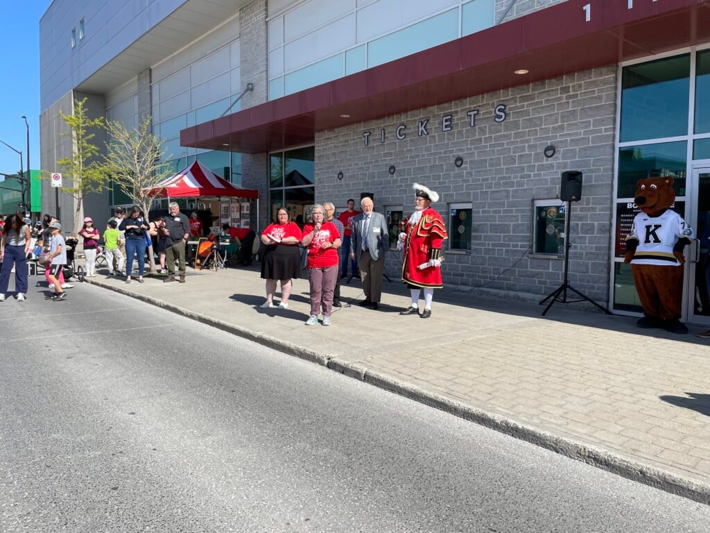 The opening ceremonies at Science Rendezvous. A group of people in red tshirts stand outside of a large building with grey brick and windows.