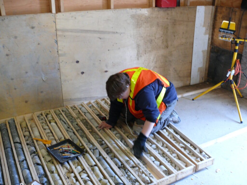 Mary-Anne is dressed in protective wear and is kneeling on a flat of rock cores.