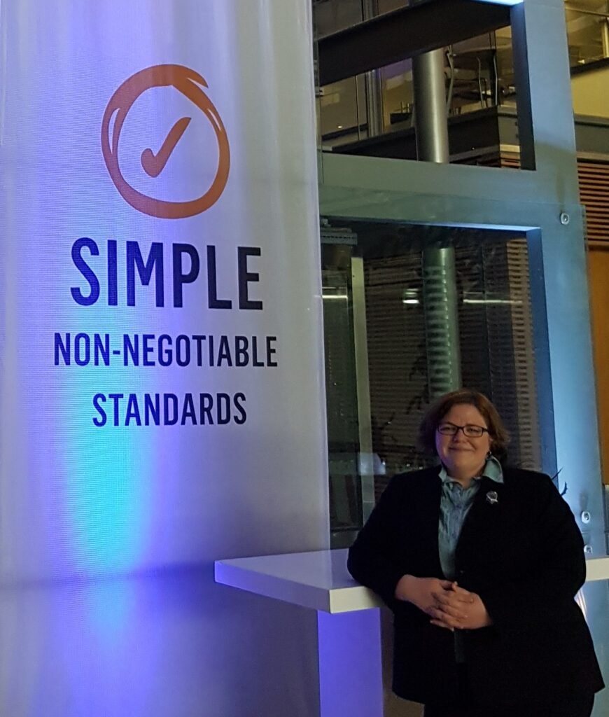 Mary-Anne stands in front of a sign that reads "Simple. Non-negotiable standards."