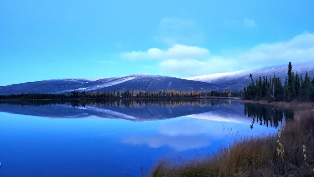 Mountains around a flat lake. The mountains are reflected in the blue water. 