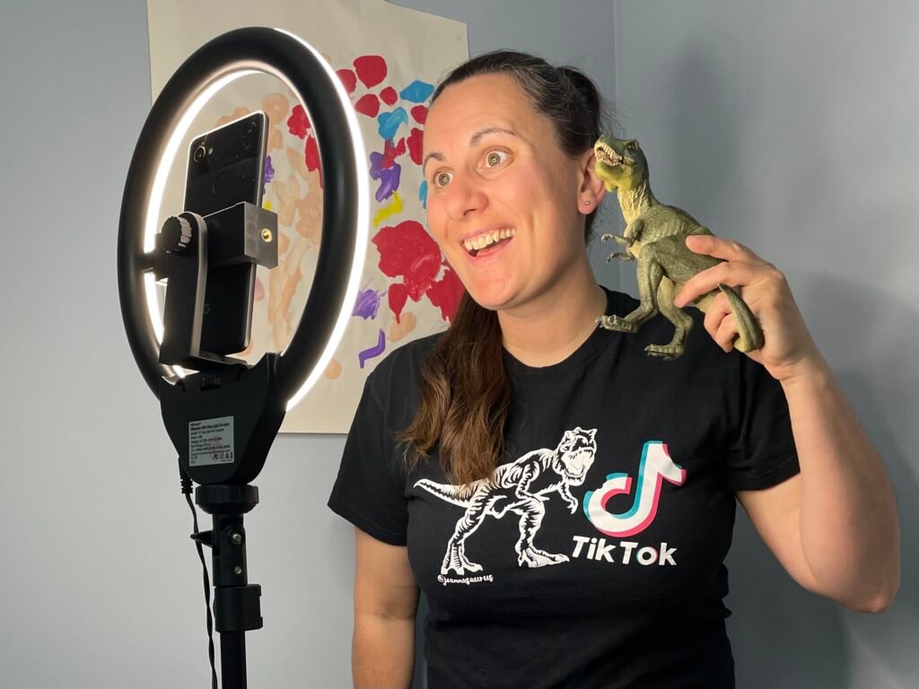 Joanna Northover posing with a toy dinosaur in front of a phone camera and ring light