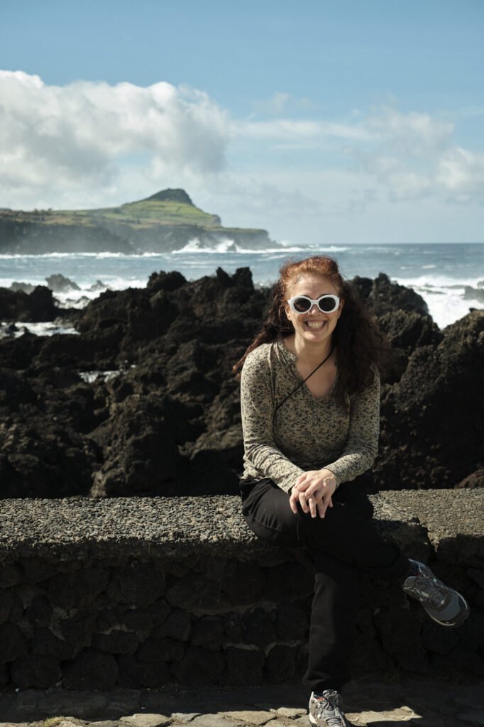 Joana Rodrigues sits on a wall with the ocean in the background